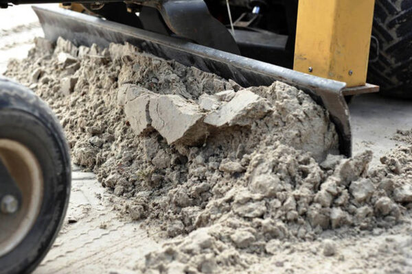 Nahaufnahme einer Schaufel, die Sand von einer Fläche abzieht und glättet