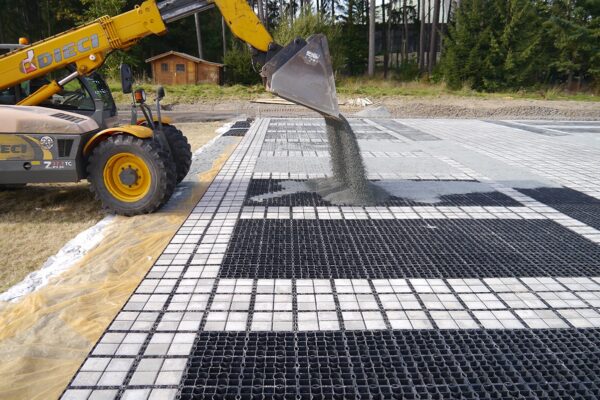 Bagger schüttet Kies auf eine leere ECORASTER Fläche.