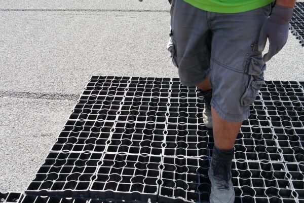 Arbeiter läuft über frisch verlegte ECORASTER Fläche, um die Elemente inneinander verrasten zu lassen.